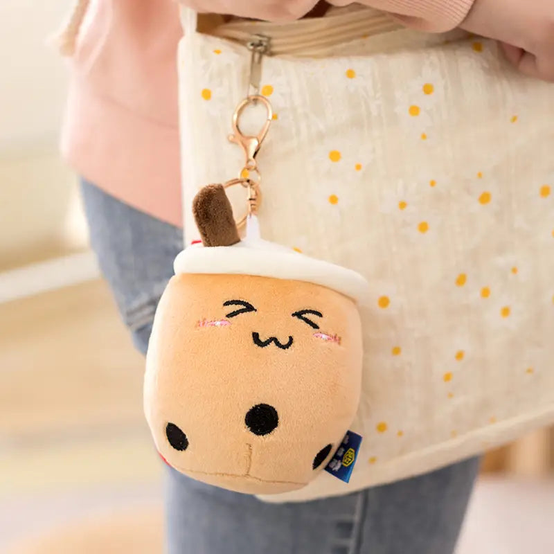 Cute beige plush boba tea keychain shaped like a milk tea cup with black tapioca pearls and an embroidered smiling face.