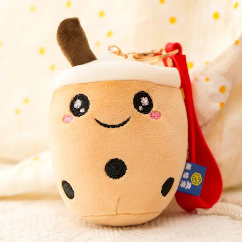Cute beige plush boba tea cup keychain featuring black tapioca pearls pink cheeks and a brown straw used as a milk tea cup doll pendant.