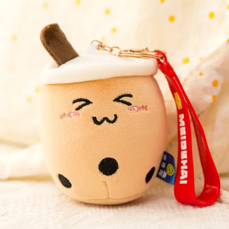 Cute beige plush boba tea cup keychain featuring black tapioca pearls white foam top and brown straw used as a milk tea cup doll pendant.