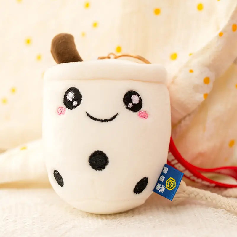 White plush boba tea plush keychain featuring a milk tea cup design with black embroidered dots, pink cheeks, and a brown straw.