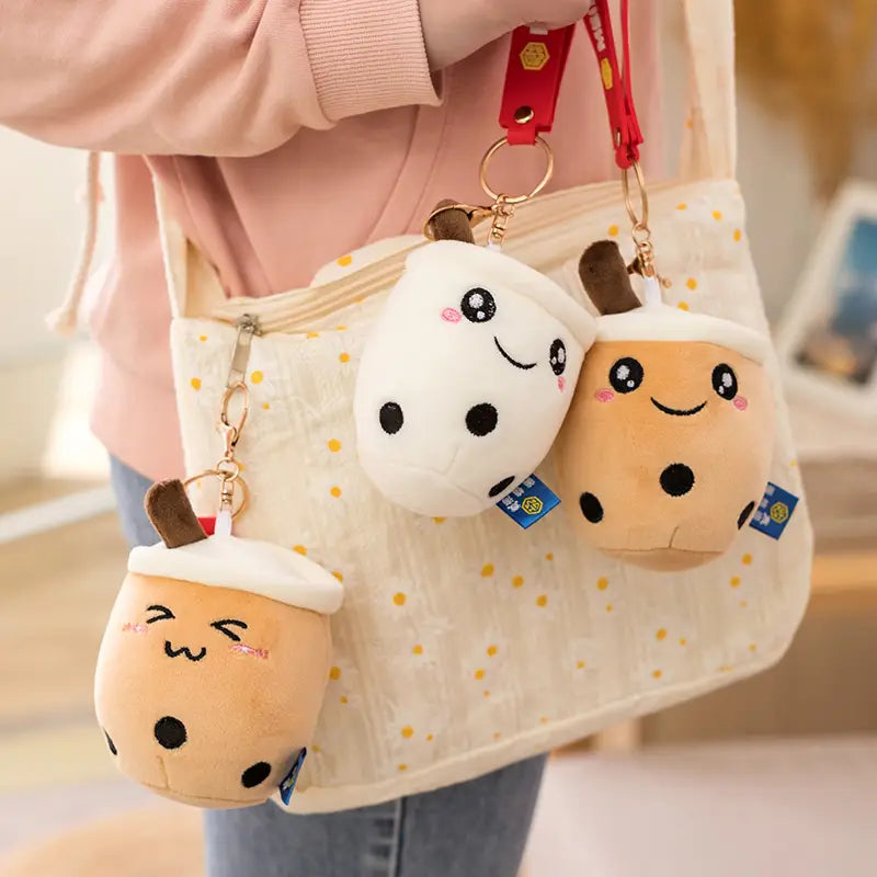 Three plush boba tea keychains in milk tea color featuring cute smiling faces and black dot details as cup doll pendants.