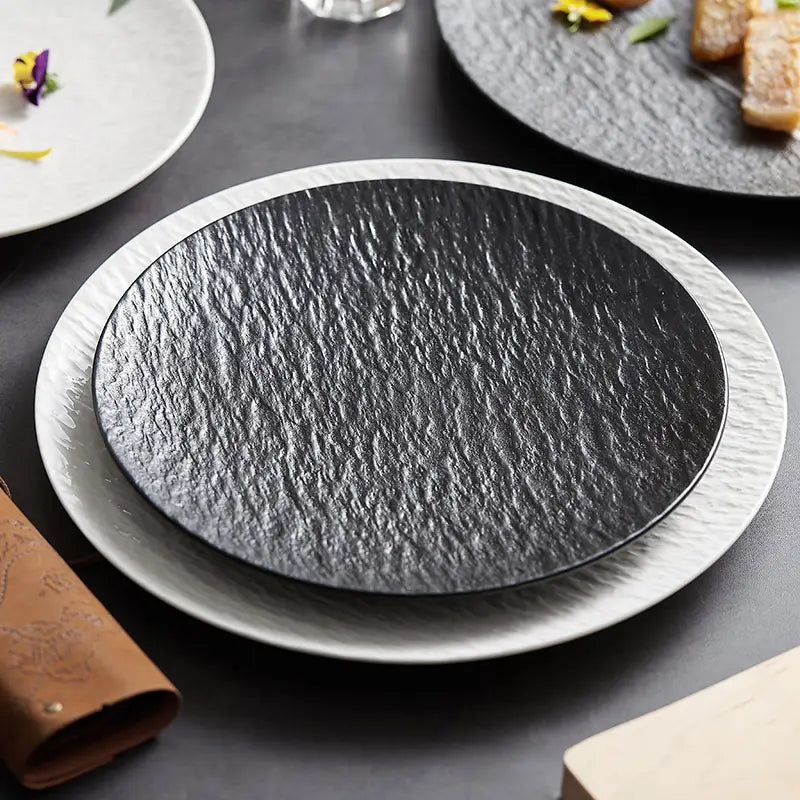 Black textured ceramic round plate with nordic rock pattern and subtle sheen resting on a white rimmed base.
