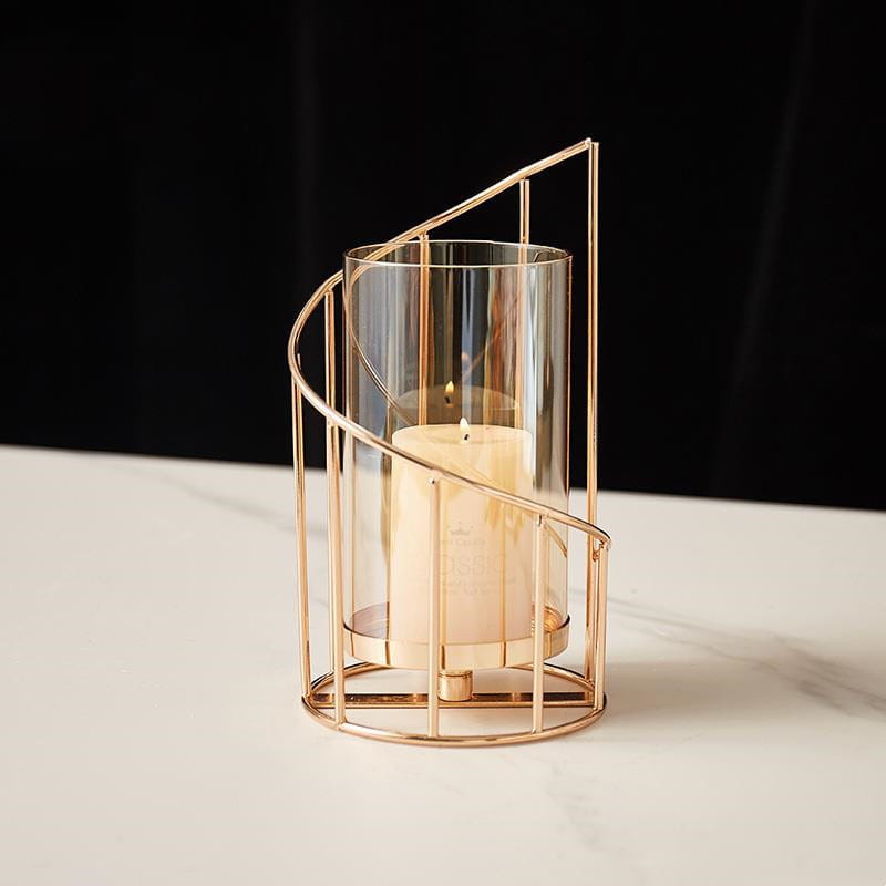 Gold metal spiral candle holder with a clear glass cylinder and a cream-colored pillar candle inside.