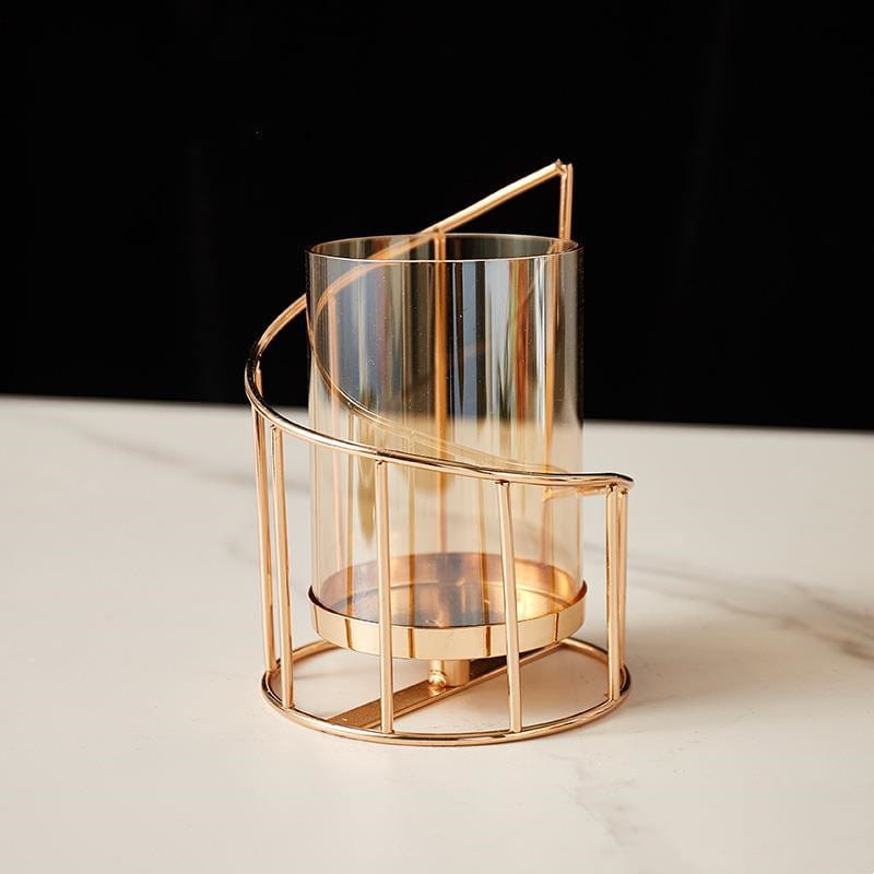 A gold metal spiral candle holder featuring a sleek metal frame cradling a clear cylindrical glass candle holder.