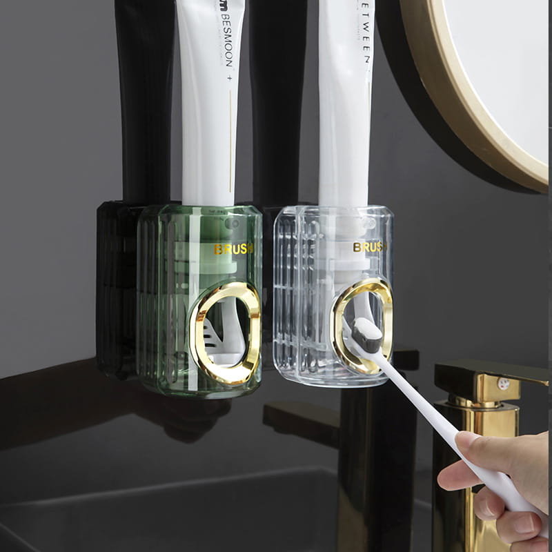 Two sleek, modern automatic toothpaste dispensers and toothbrush holders in translucent green and clear colors with gold-accented circular openings for dispensing toothpaste.