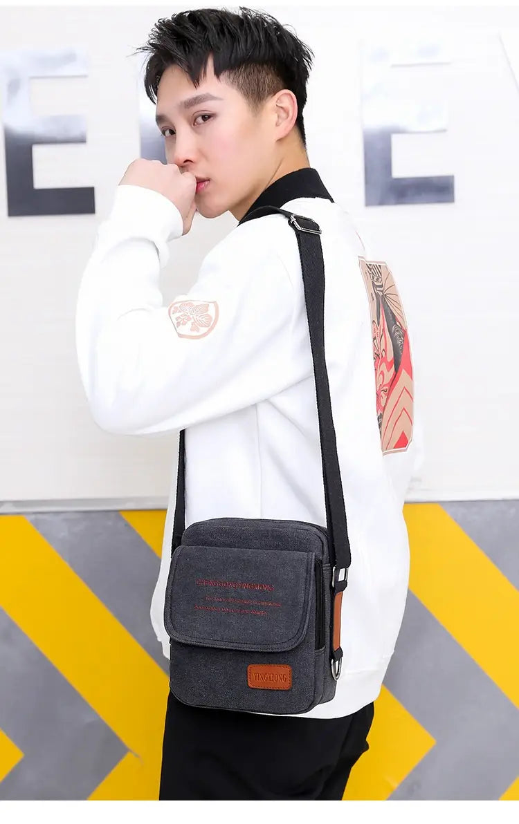 Men’s dark gray canvas crossbody business shoulder bag with a brown leather patch and black strap.