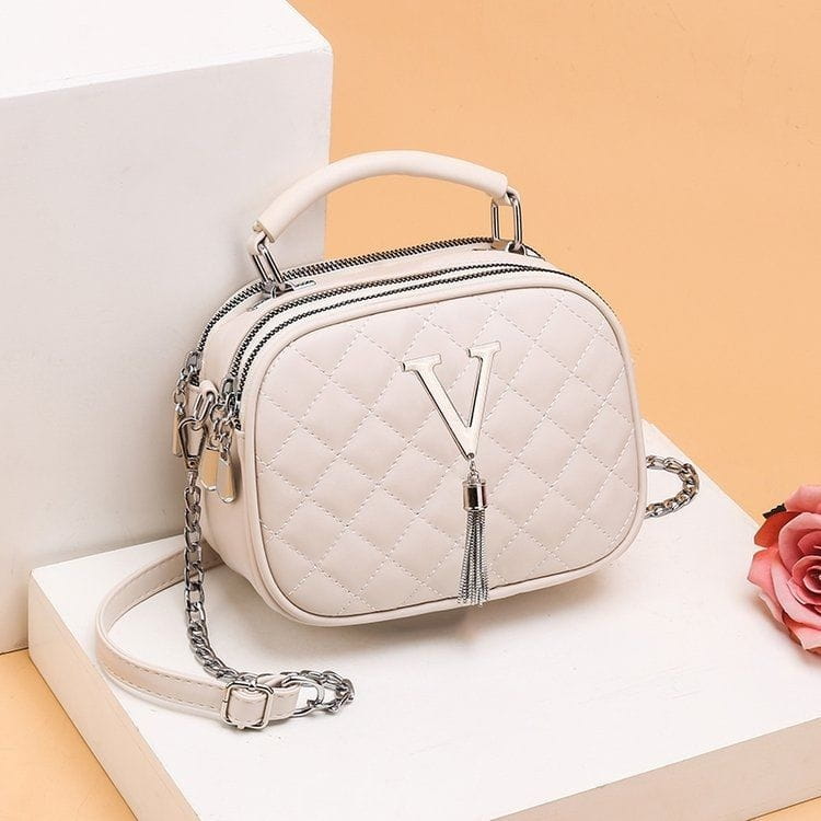 White quilted handbag with silver v logo and tassel featuring a chain-and-leather strap