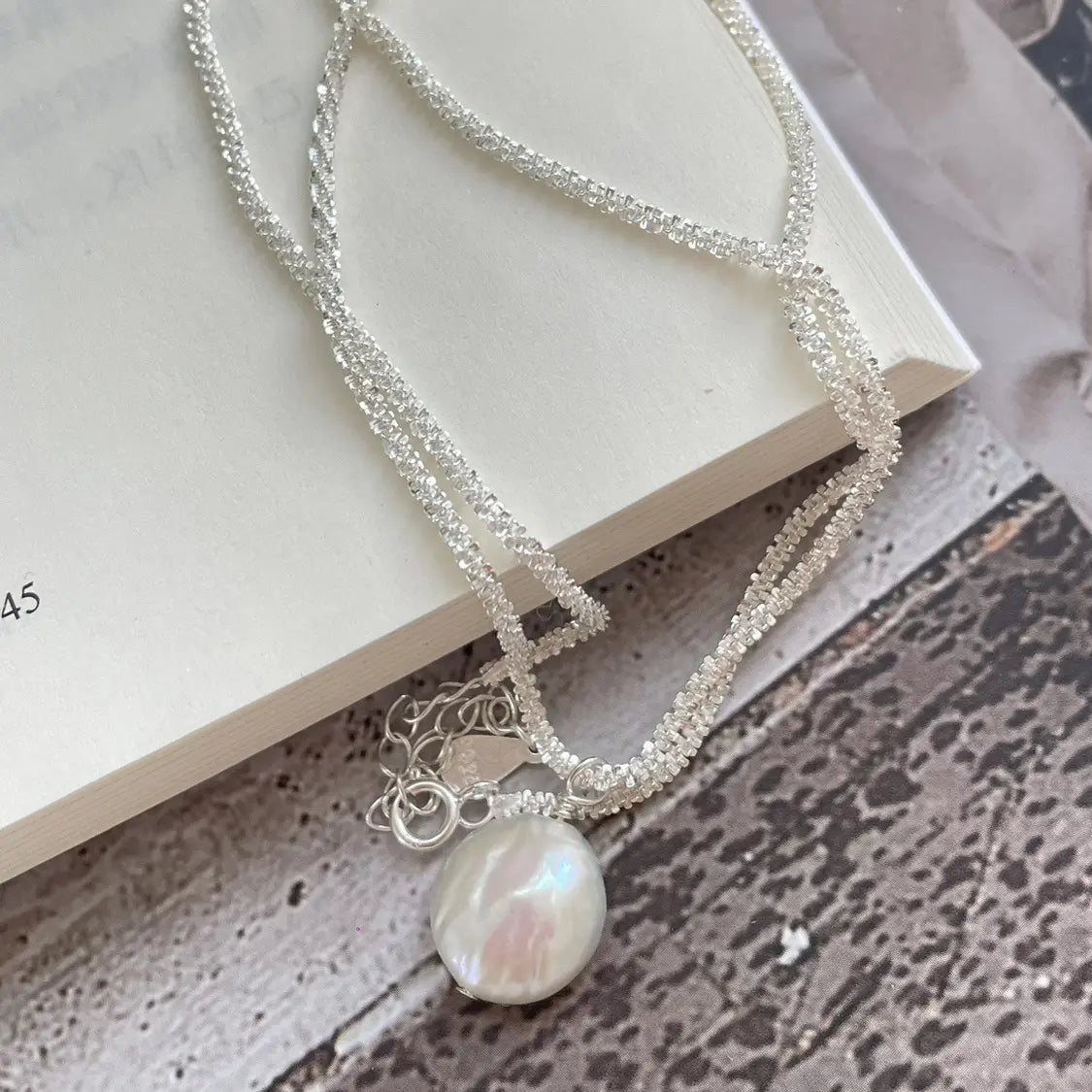 A sterling silver chain necklace featuring a delicate baroque pearl pendant with lustrous white and subtle iridescent overtones.