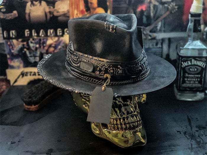 A dark distressed leather plush skull cowboy hat featuring intricate silver toned metal detailing and a decorative band.