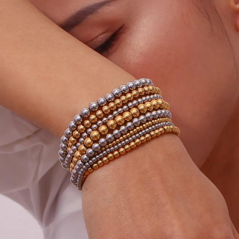 Stacked multi-layer 18k gold plated stainless steel elastic bead bracelet featuring alternating gold and silver metallic spheres.