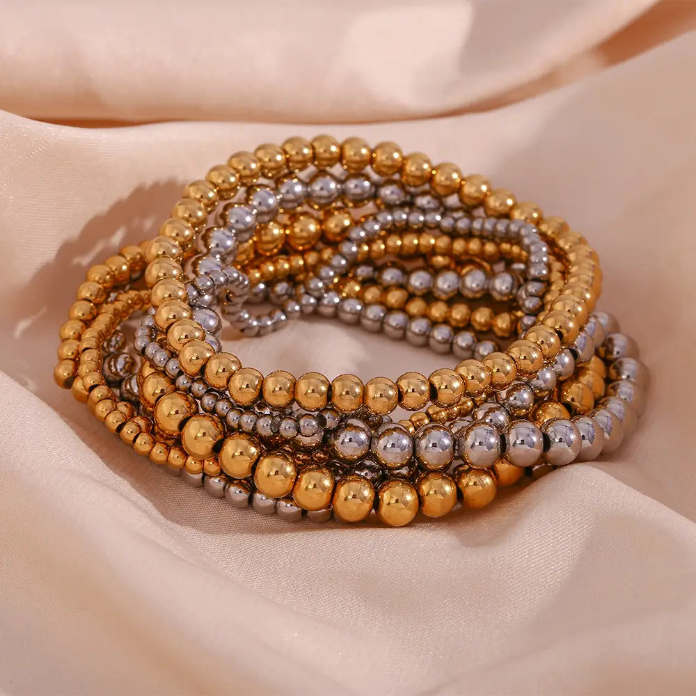 Stacked gold and silver beaded stretch bracelets made of 18k gold plated stainless steel elastic beads.