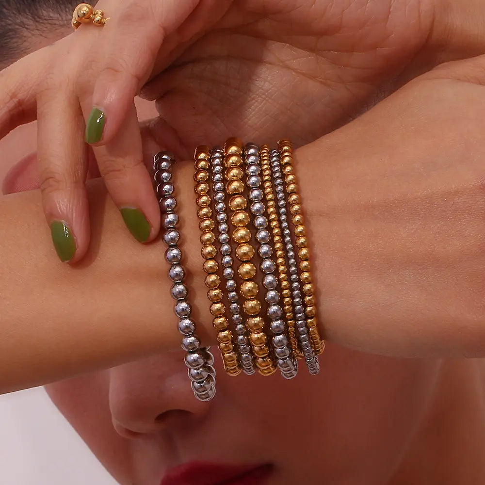 A set of five 18k gold plated stainless steel elastic bead bracelets in gold and silver tones featuring uniformly sized polished spherical beads.