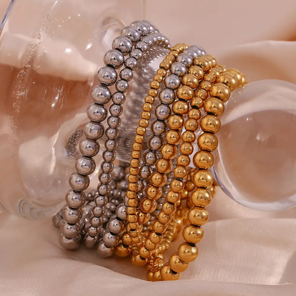 Stacked metallic beaded bracelets in polished silver and gold tones featuring 18k gold plated stainless steel with an elastic design.