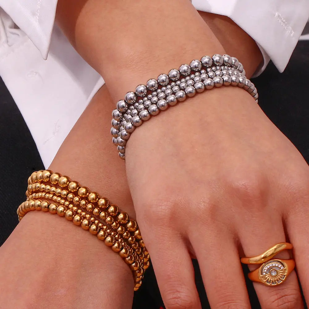 Stacked silver and gold 18k gold plated stainless steel elastic bead bracelets with a polished metallic finish.