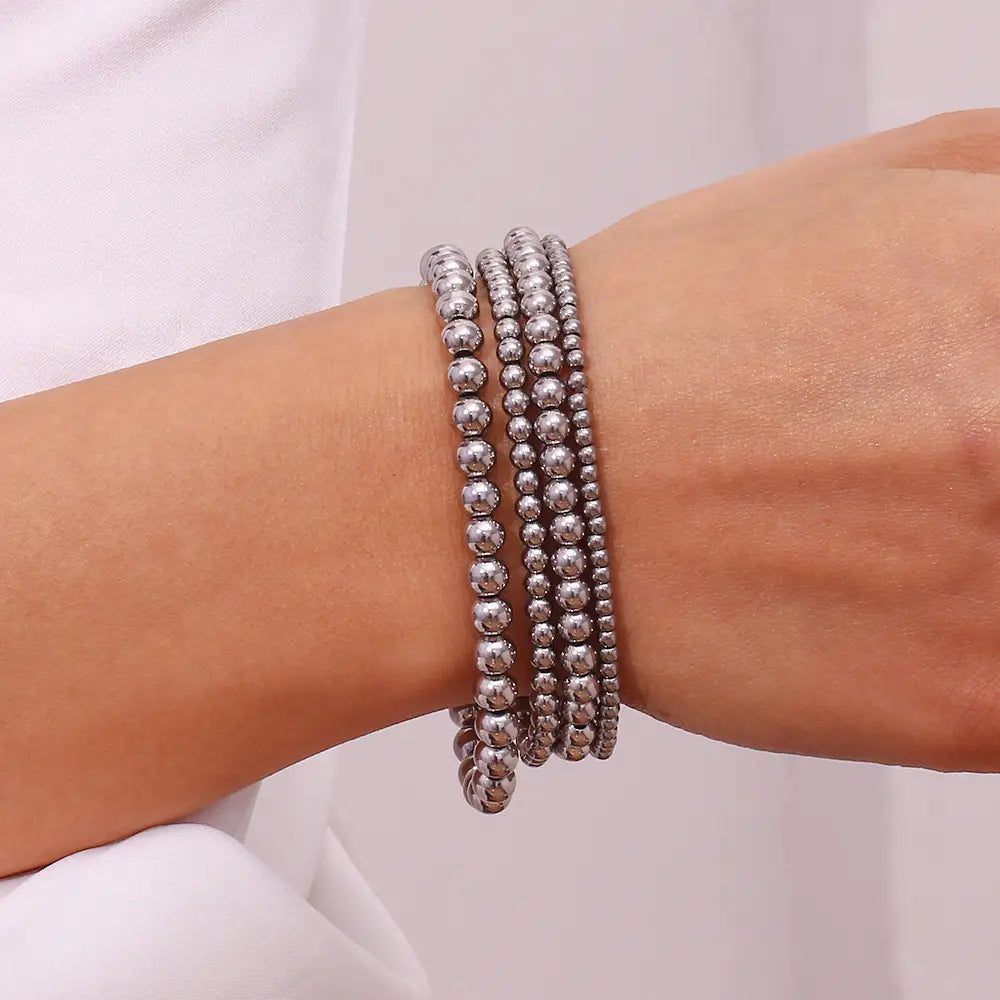 A silver beaded 18k gold plated stainless steel elastic bead bracelet worn on wrist.