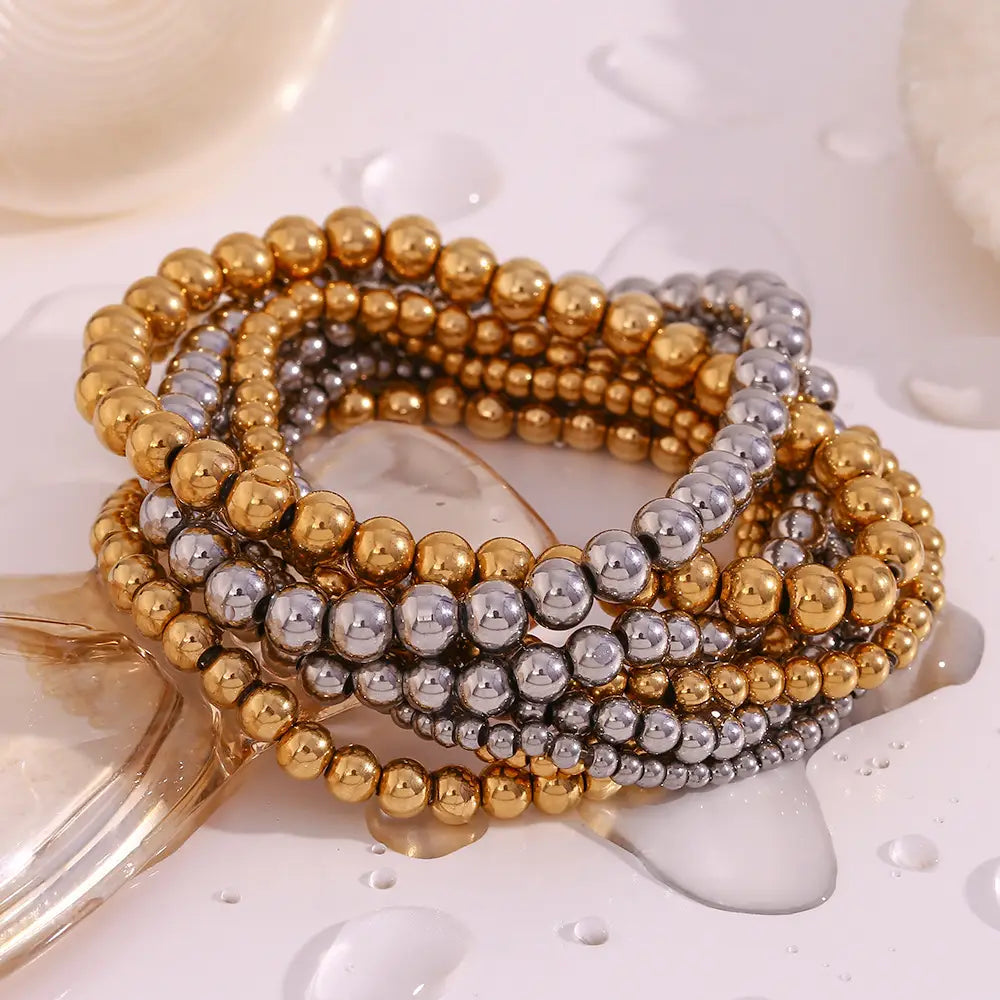 Stacked gold and silver metallic bead bracelets made of 18k gold plated stainless steel with elastic design.
