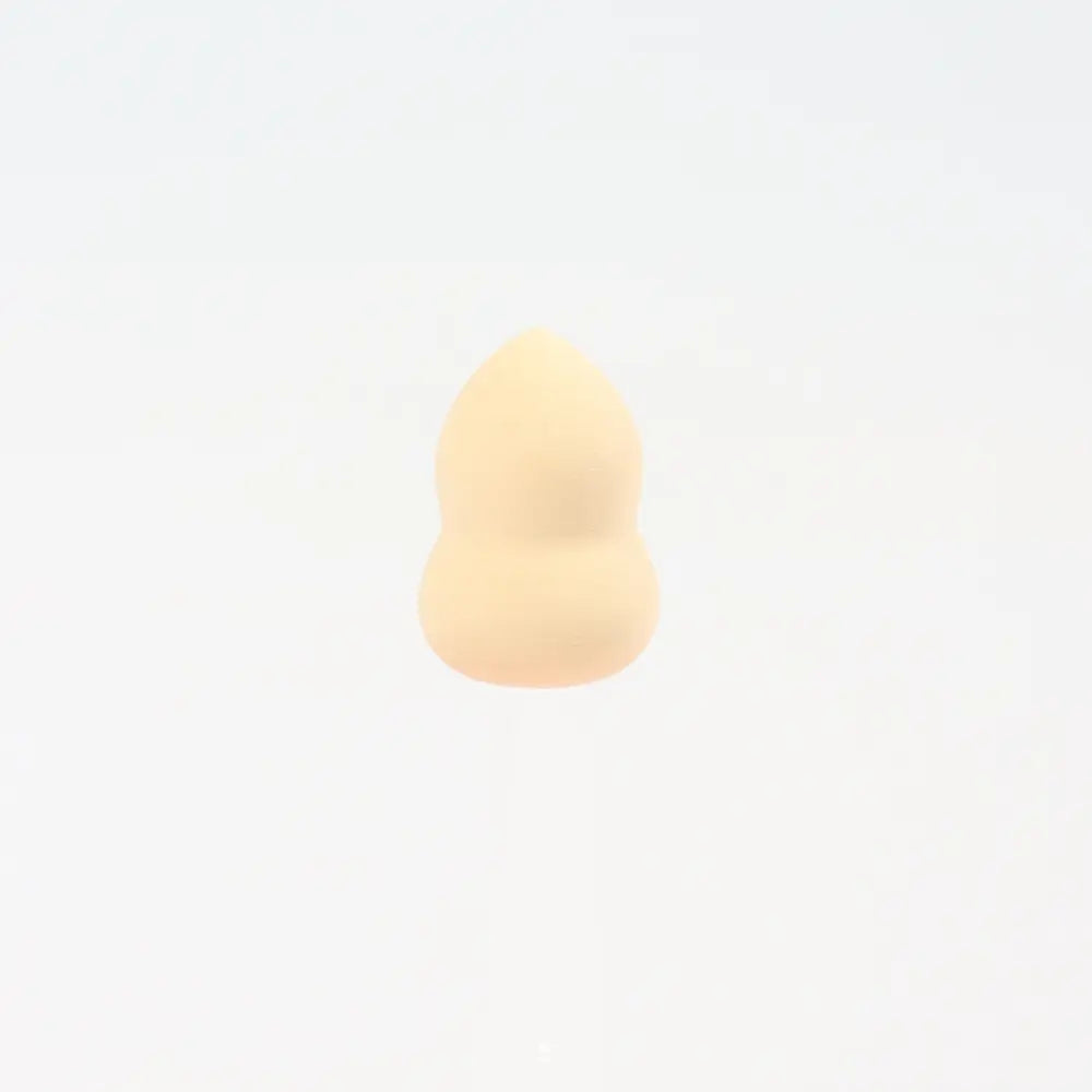 Une mini éponge de maquillage en silicone beige, de forme goutte arrondie et douce, pour une application du fond de teint parfaitement lisse.