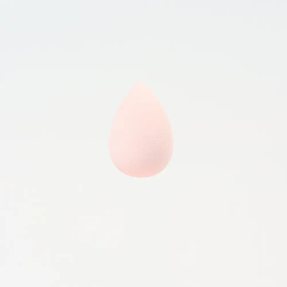 Une mini éponge de maquillage rose pâle en forme de goutte, à finition mate lisse, conçue pour un estompage précis du maquillage.