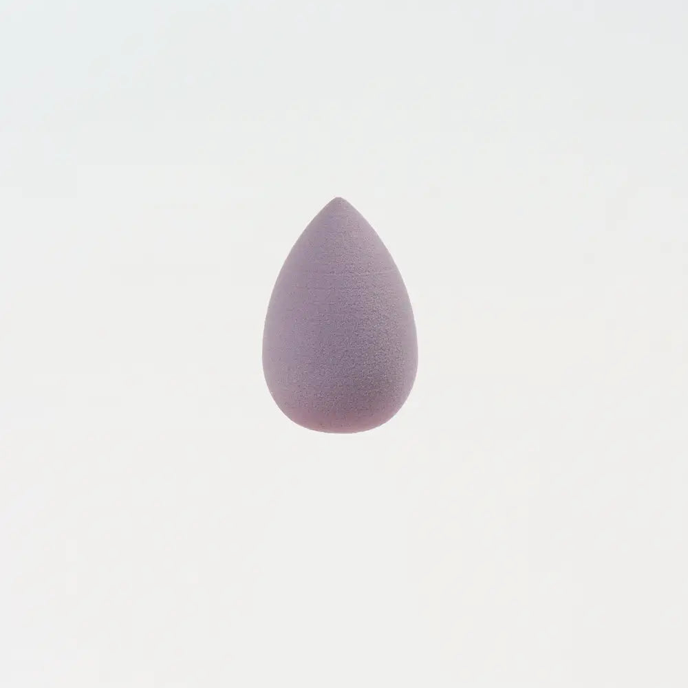 Une mini éponge de maquillage lilas doux, de forme goutte, à texture poreuse lisse, conçue pour un estompage précis du maquillage.