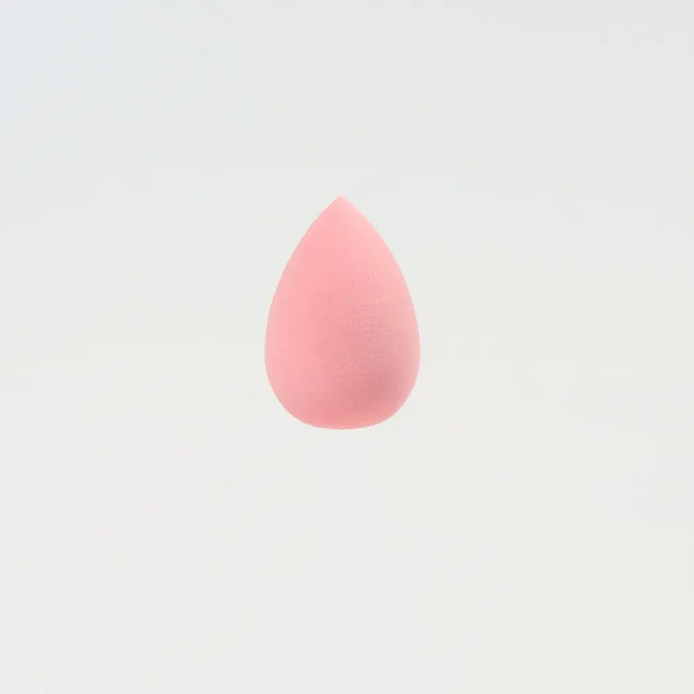 Une mini éponge de maquillage rose pâle en forme de goutte, à finition mate lisse, conçue pour estomper et appliquer des produits de beauté.