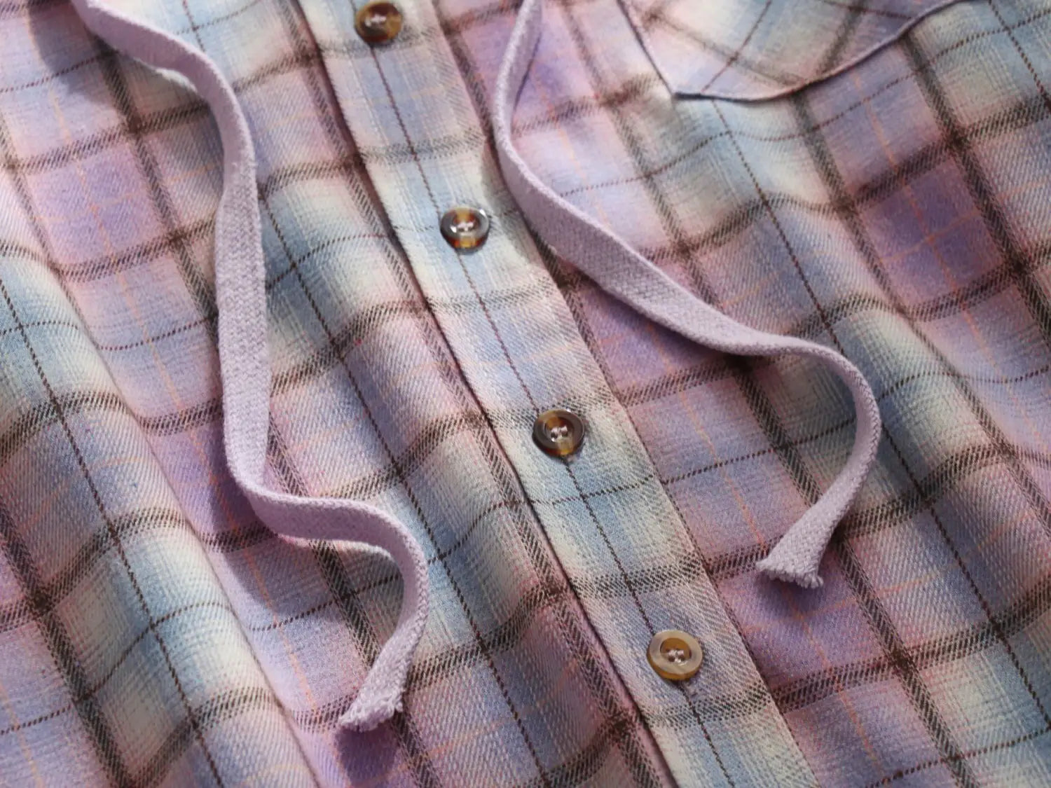 Women’s plaid long sleeve hooded button up shirt in soft pastel flannel with pink lavender and light blue hues featuring brown wooden buttons and matching drawstrings