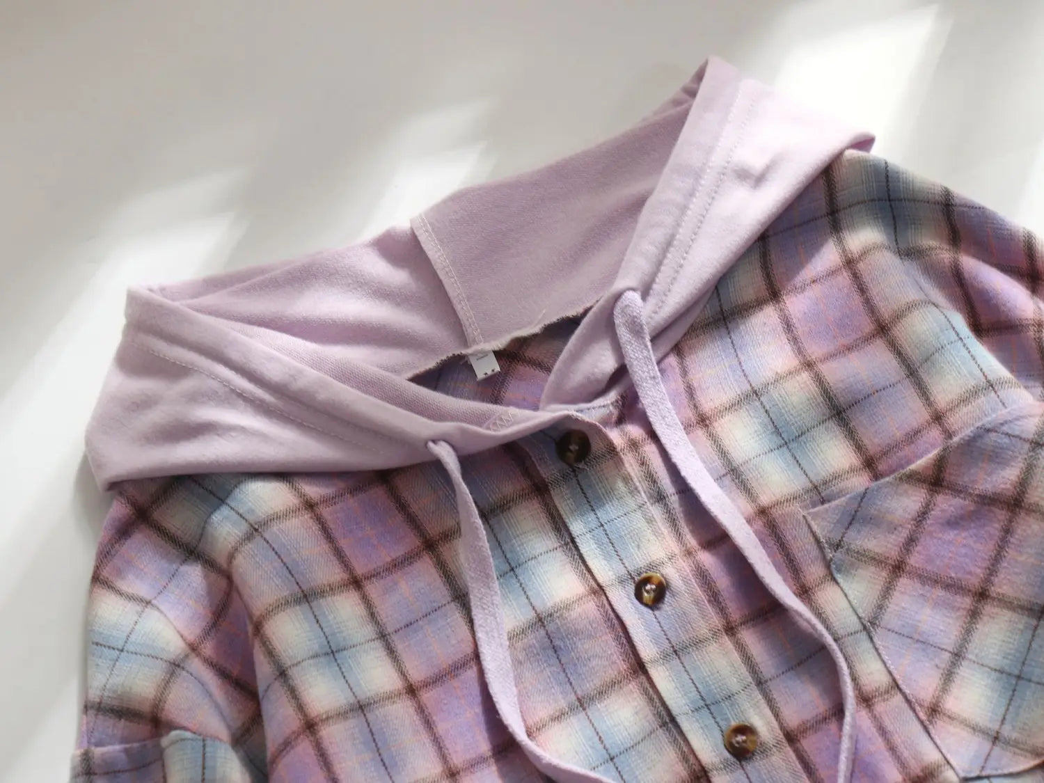Women’s plaid long sleeve hooded button up shirt in soft lavender and pastel plaid with a matching drawstring hood and subtle button closures.