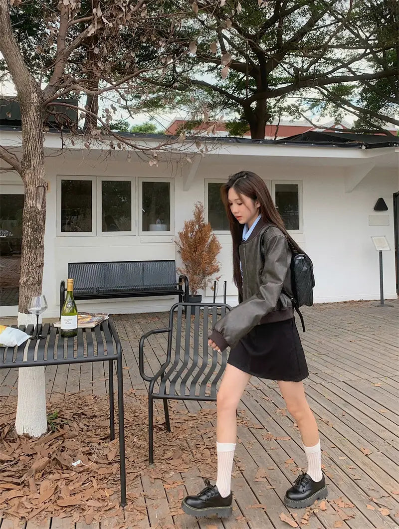 Black leather backpack with a minimalist design and subtle stitching details shown from the back paired with a faux leather bomber jacket retro biker style.