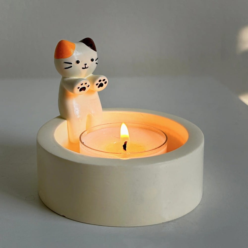 Cute white orange and black ceramic cat figurine perched atop a circular candle holder in the cat candlestick holder ceramic kitten tea light stand product.