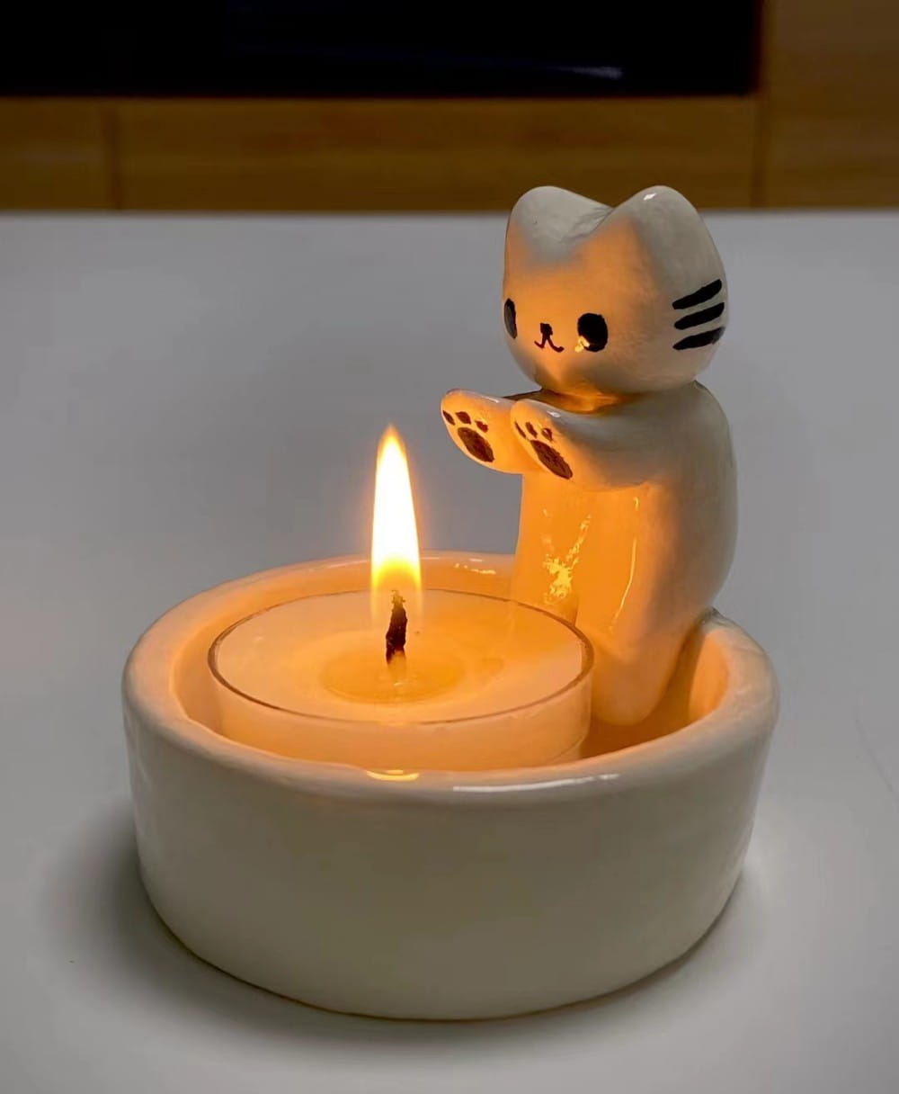 Ceramic cat candlestick holder with a white glossy finish and black whiskers featuring paw prints on its front paws for holding tea light candles.