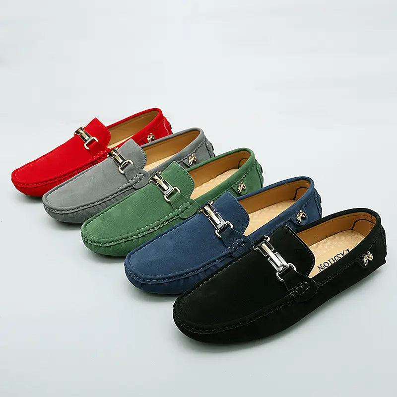 Eine Reihe handgefertigter Herren-Slipper aus Samtleder mit Horsebit-Design in Rot, Grau, Grün, Blau und Schwarz, mit silberfarbenen Metall-Schnallen.