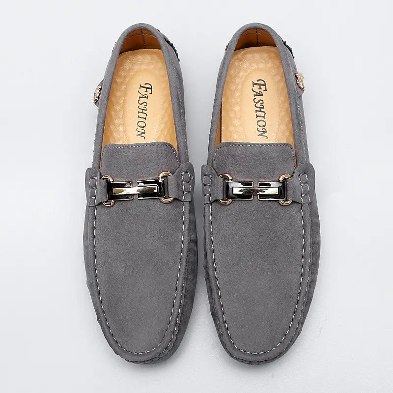 Herren-Slipper aus Samtleder mit Horsebit-Design in Grau, mit metallischen Schnallenakzenten und weißer Ziernaht, handgefertigt als Gommino-Schuh.