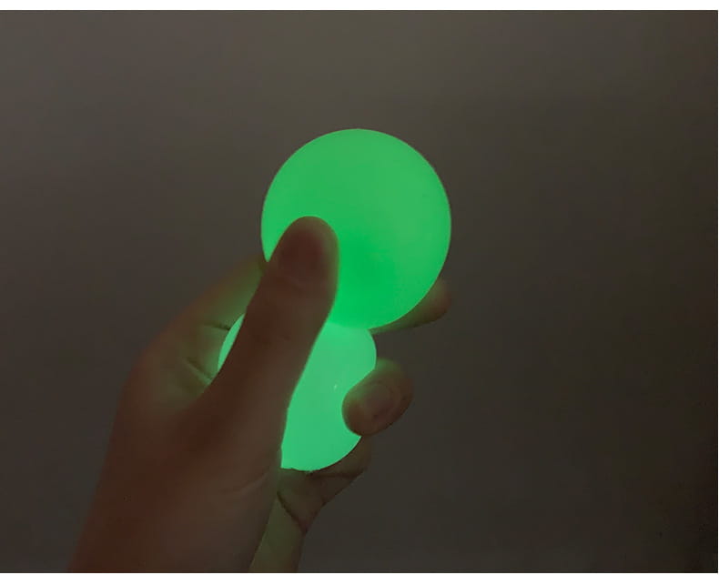 A glowing green luminous sticky wall ball held in a hand designed as a glow in the dark squeeze toy.