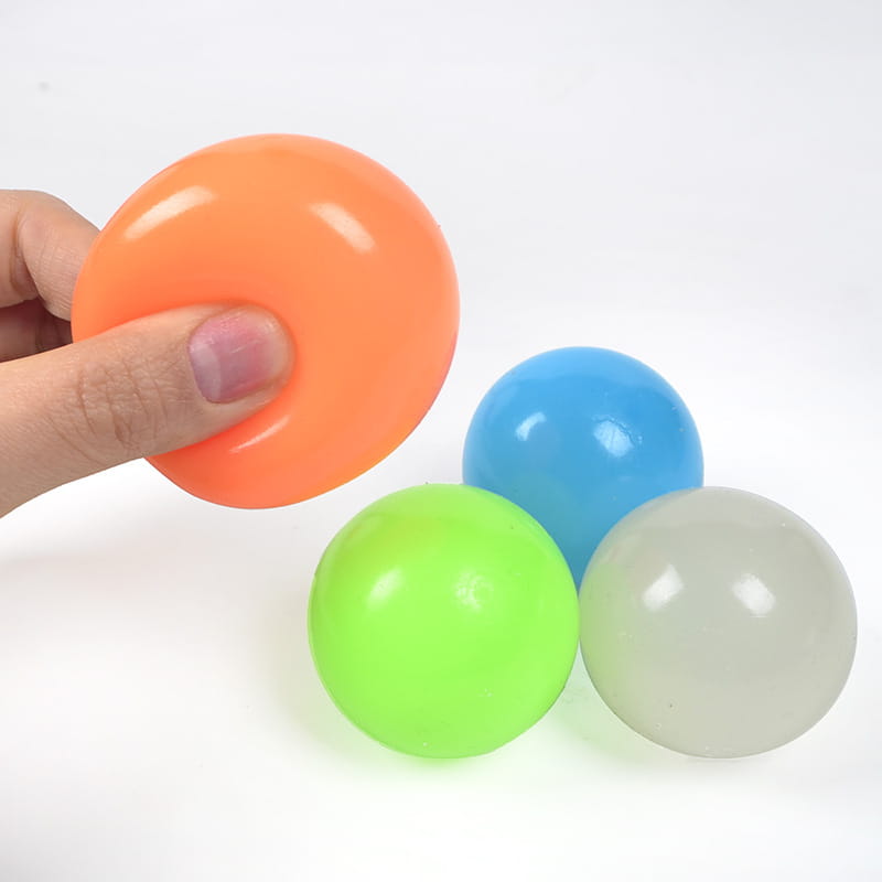 A hand holding an orange translucent plastic stress ball from the luminous sticky wall balls glow in the dark squeeze toy collection.