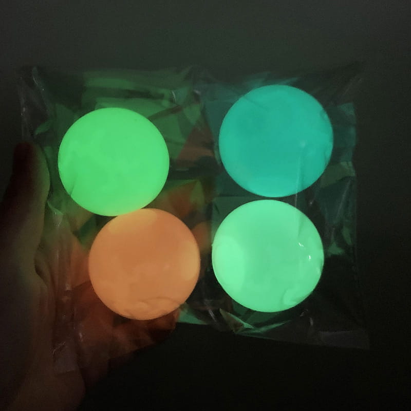 A clear plastic bag containing three glowing green and one orange luminous sticky wall balls glow in the dark squeeze toys.