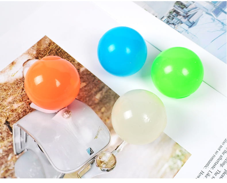 four glossy luminous sticky wall balls in orange blue green and translucent white arranged on a surface glow in the dark squeeze toy