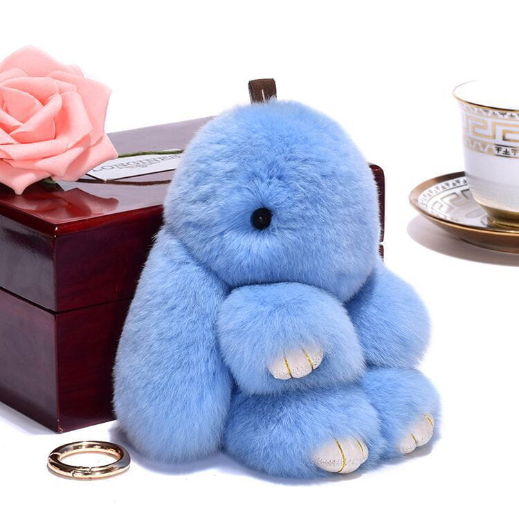 A soft light blue fluffy rabbit plush keychain with black eyes white paw pads and gold stitching accents measuring 15cm.