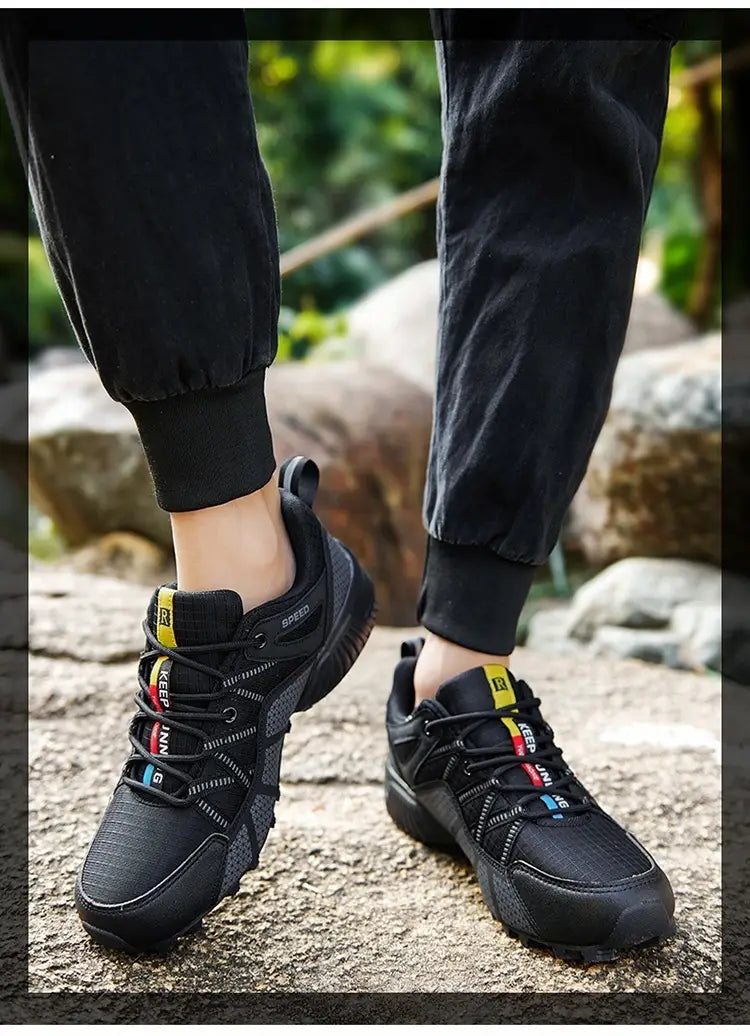 Men’s breathable mesh trail running and hiking shoes in black with vibrant yellow and blue accents on the laces and tongue, featuring a rugged mesh upper and durable rubber sole.