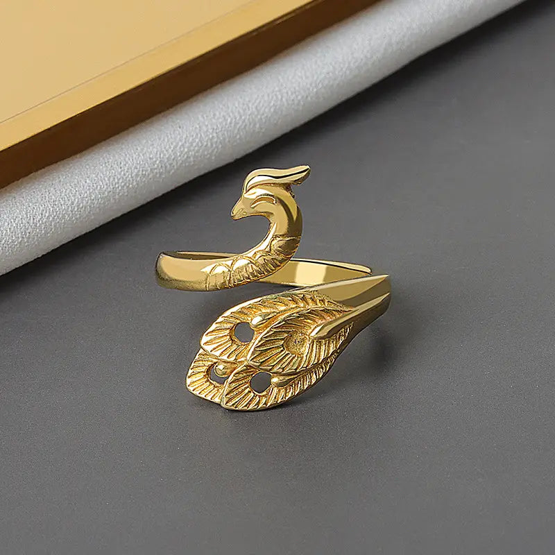 Gold-colored adjustable peacock and fish crochet tension ring with intricate feather detailing and a sleek band.