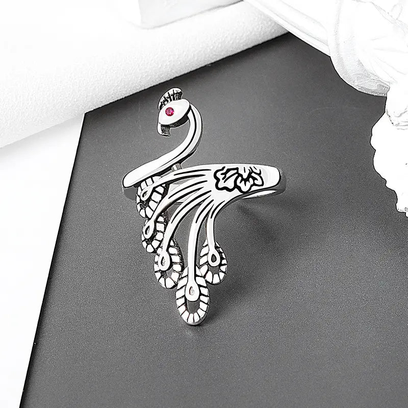 adjustable silver peacock ring featuring a red gemstone eye and intricate feather detailing for use as a crochet tension ring.