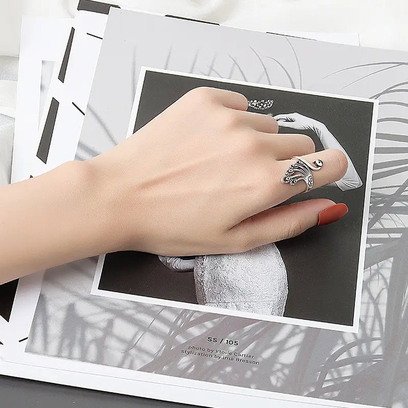 a silver-toned adjustable peacock and fish crochet tension ring with an intricately designed swirling pattern and small embellishments adorning the finger