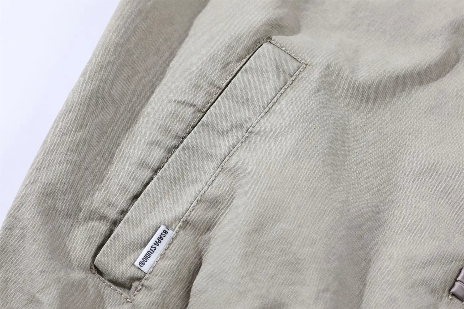 Une poche en toile beige avec des coutures soignées et une petite étiquette de marque blanche sur une veste rétro pour homme de style chinois.