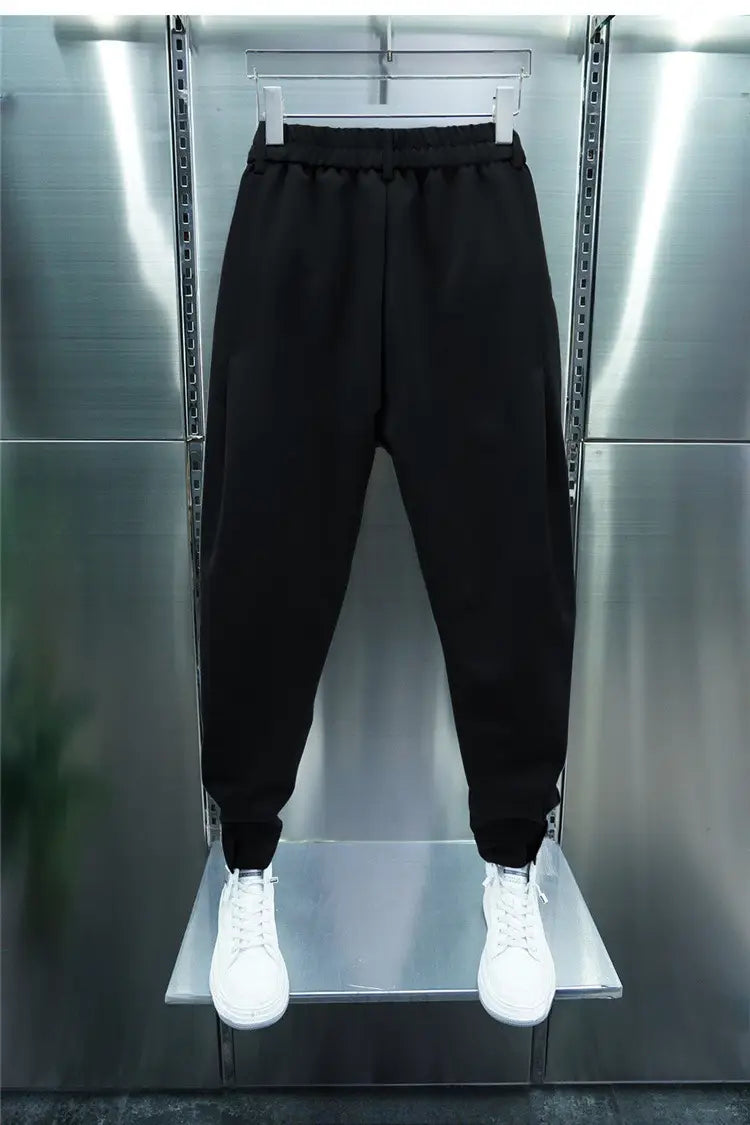Men’s casual tapered jogger pants made of black cotton with an elastic waistband and ribbed cuffs displayed on a hanger against a metallic background.