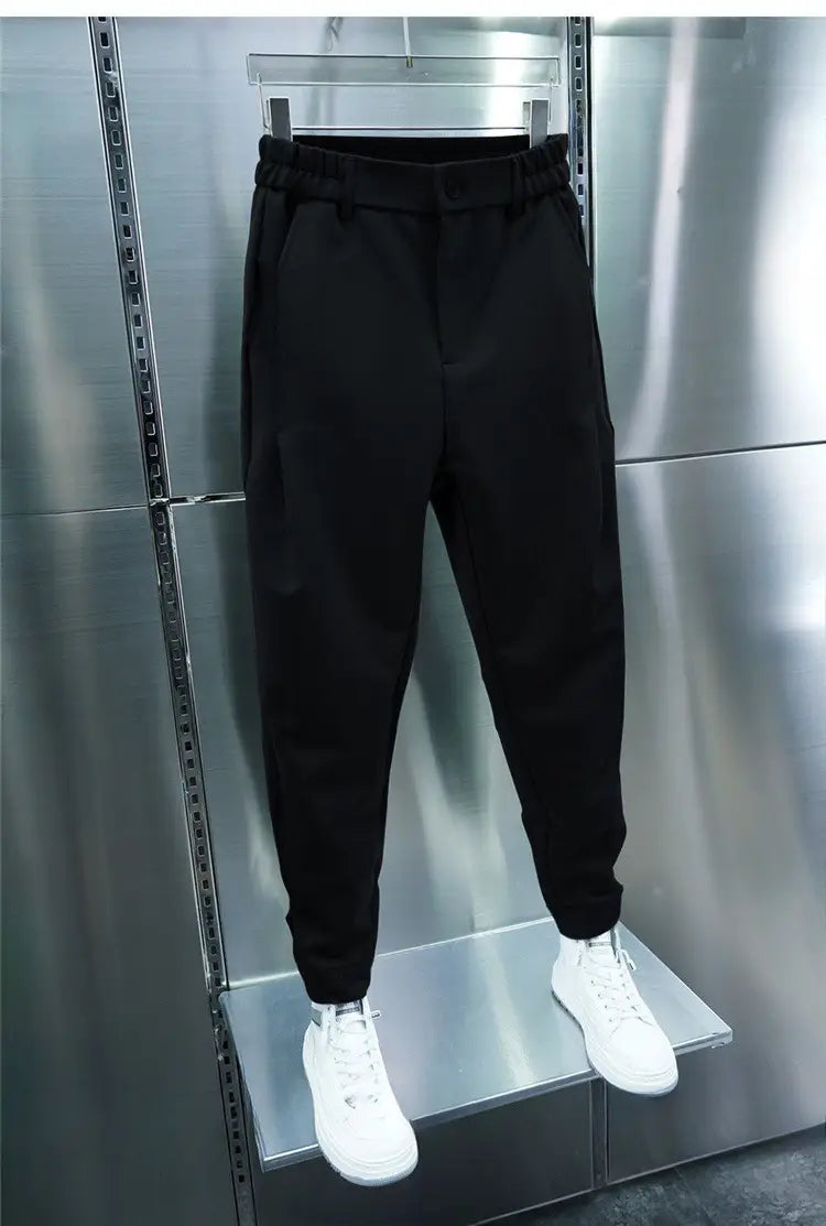 Men’s casual tapered jogger pants in black with an elastic waistband and ribbed cuffs displayed on a hanger against a metallic backdrop.