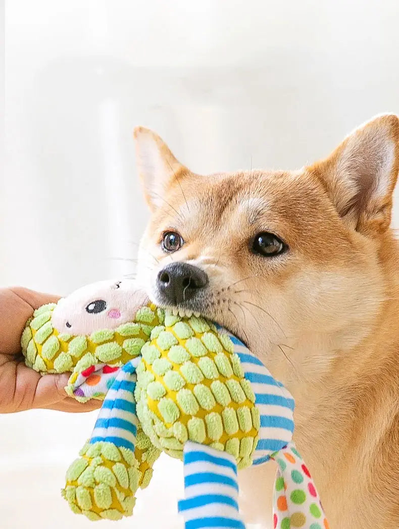 Ein Plüsch-Grün- und Gelb-Korn-förmiges Quietsch-Hundespielzeug aus weichem Stoff mit blauen und weißen gestreiften Schleifchen, entworfen für interaktives Kauen.