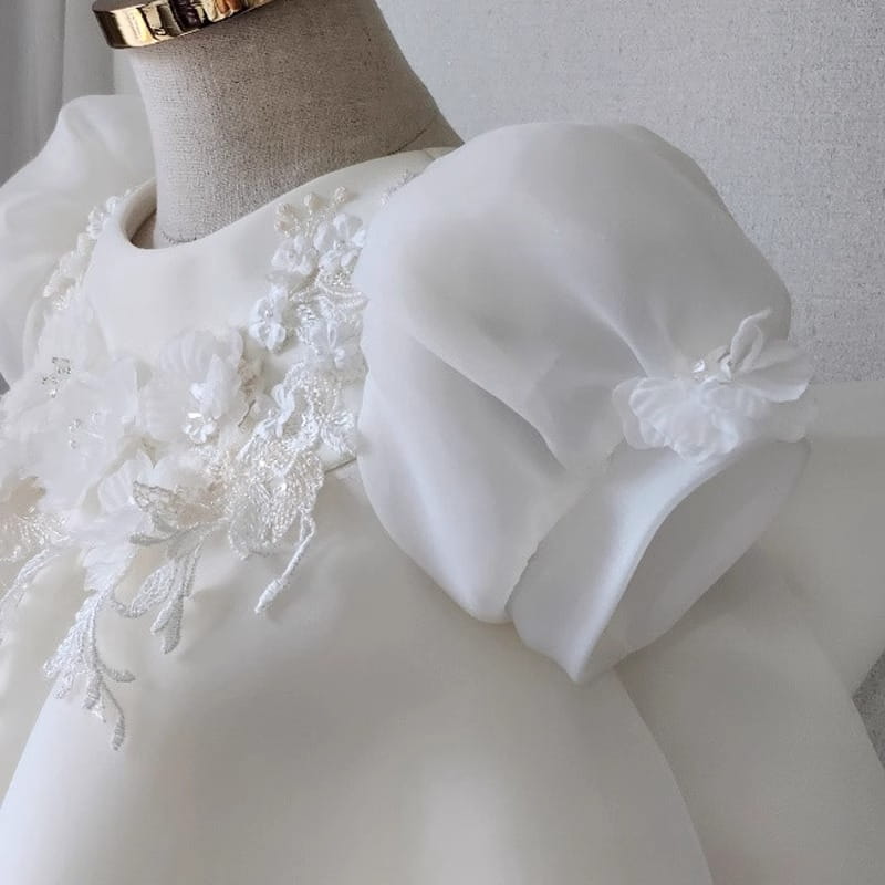 Robe de mariée princesse en dentelle florale blanche pour filles, présentant une robe en satin blanc élégante avec des appliqués délicats en dentelle florale et une manche bouffante en organza transparent volumineux.