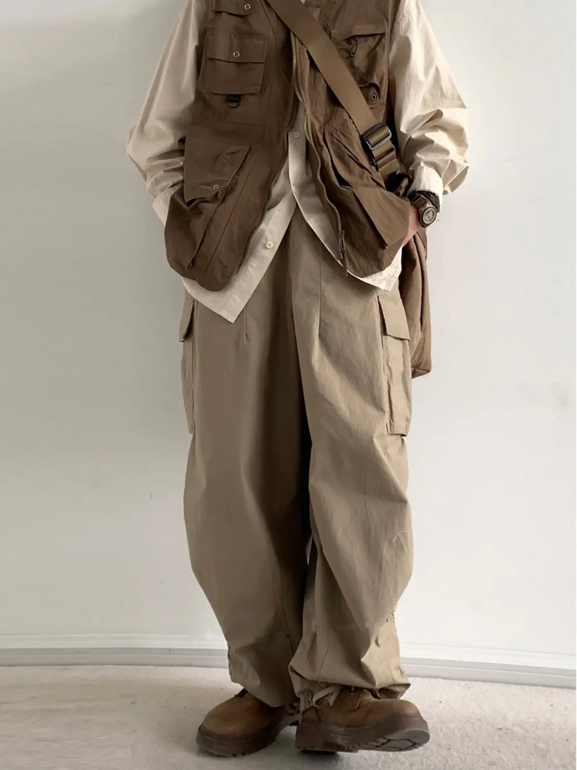 Gilet utilitaire en beige avec plusieurs poches et une bandoulière réglable, associé à un pantalon cargo ample japonais rétro en tissu confortable.