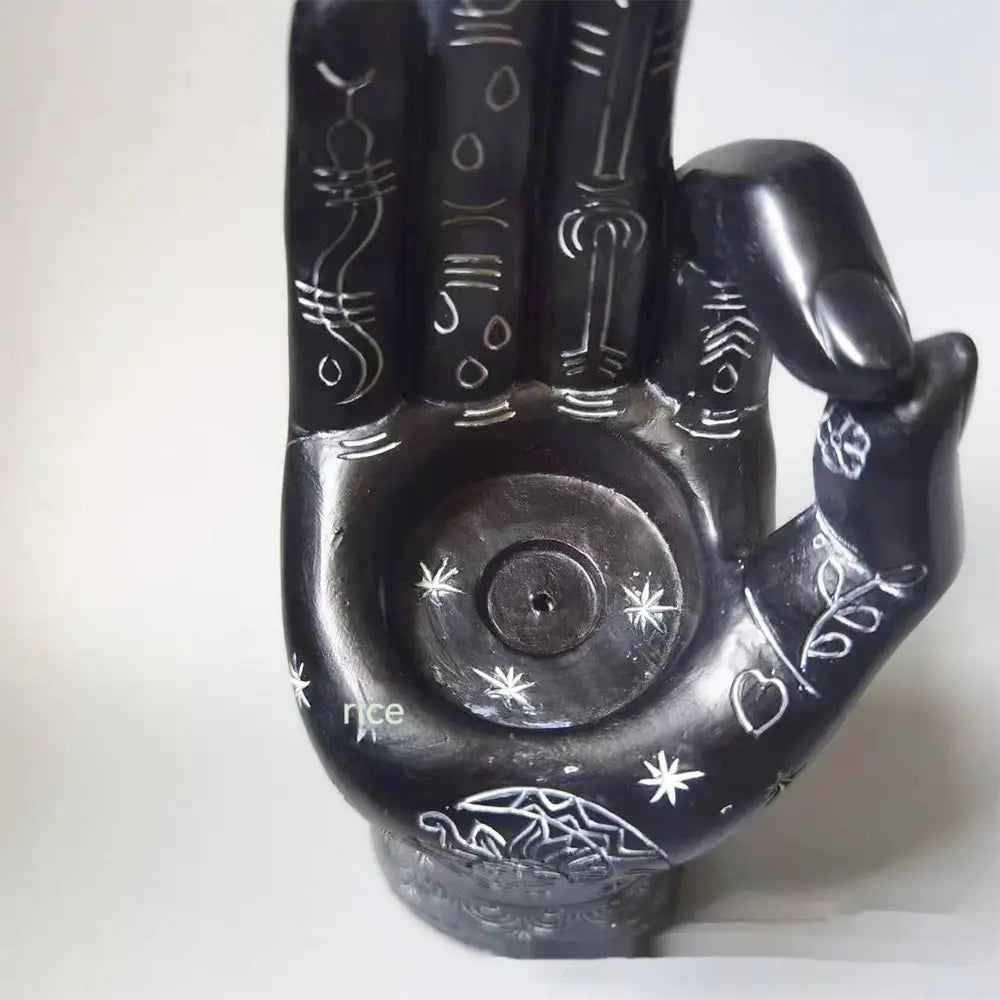 Black hamsa hand-shaped incense burner and candle holder figurine with intricate white engraved symbols and star patterns.