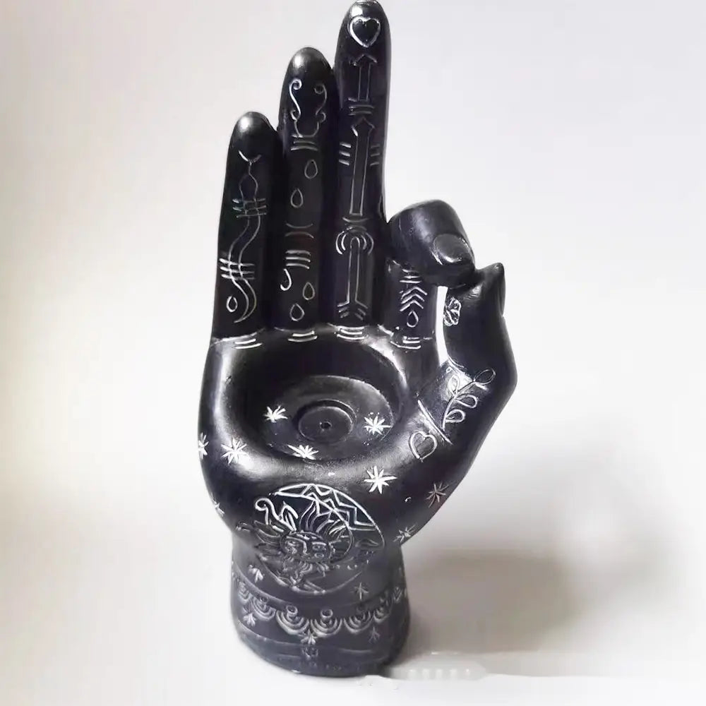Black hand-shaped incense burner and candle holder figurine with intricate white engraved designs and patterns on the front side.