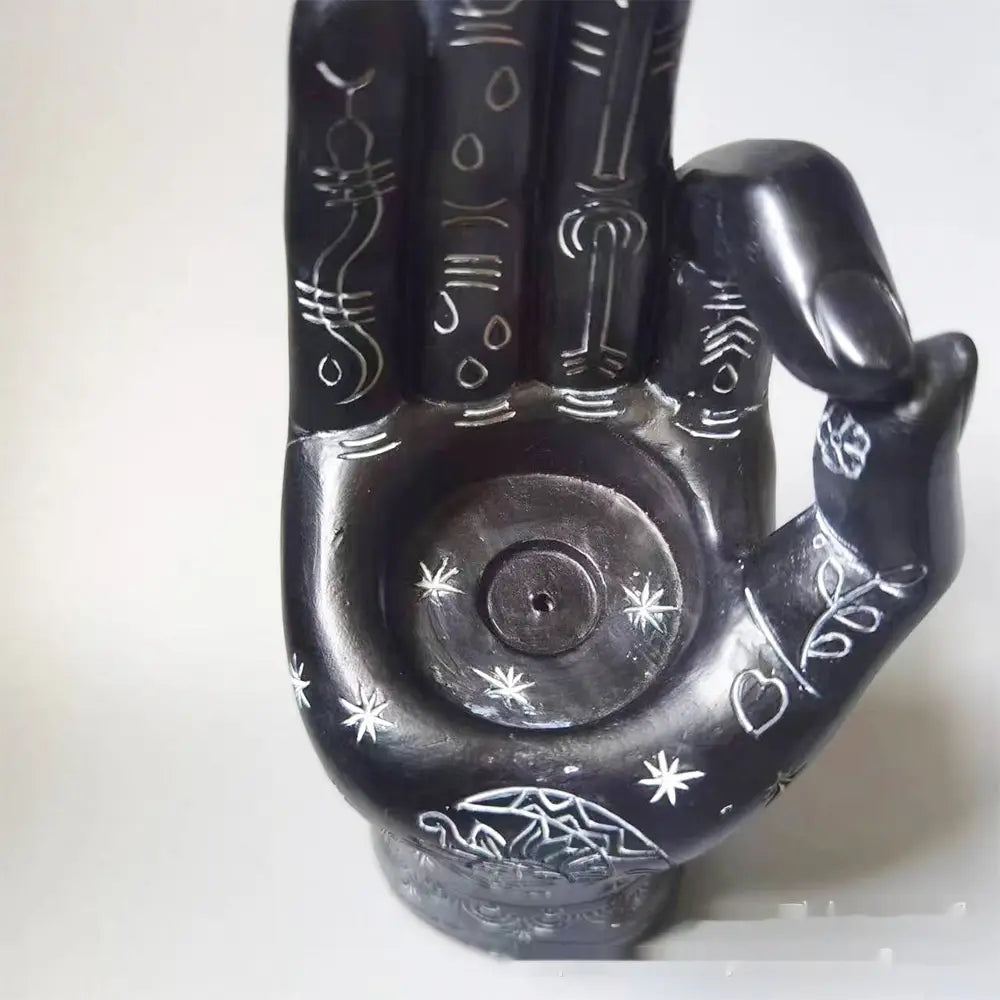 Black hamsa hand incense burner and candle holder figurine with intricate white engraved symbols and star patterns featuring a central circular indentation for holding incense or small objects.