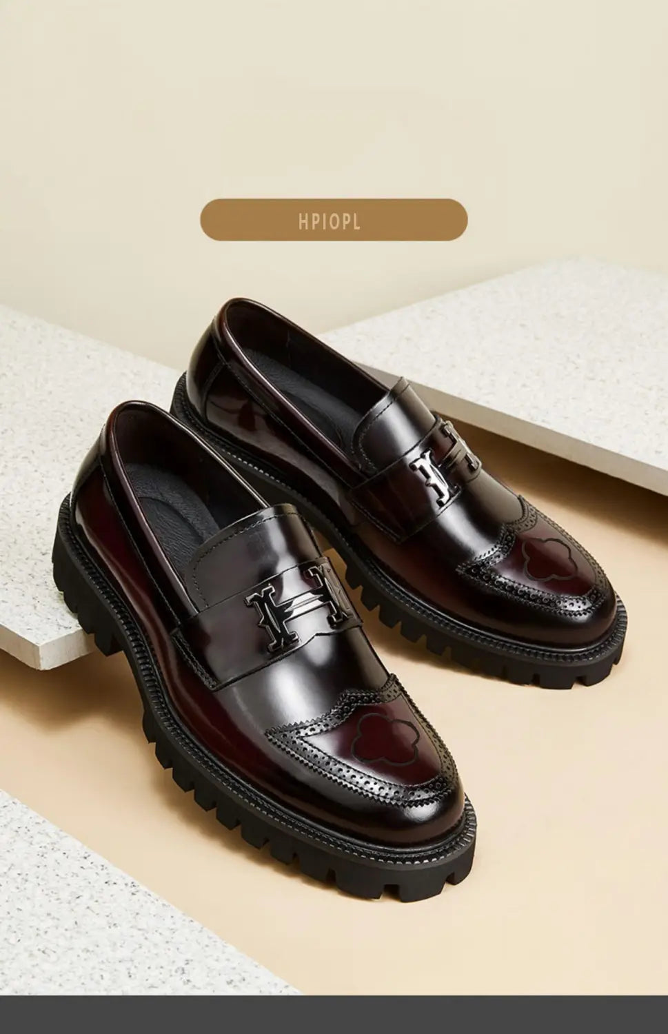 Mocassins en cuir bordeaux avec une finition vernie brun foncé lustrée, des boucles métalliques noires en forme de H, des détails brogue complexes au niveau de l’avant-pied, et une semelle en caoutchouc.